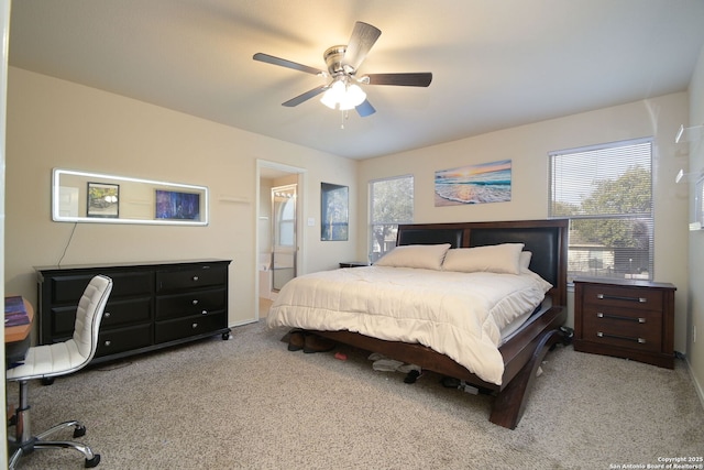 carpeted bedroom with ensuite bath, multiple windows, and a ceiling fan