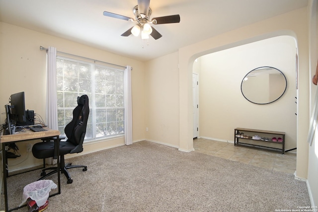 carpeted home office with tile patterned floors, baseboards, arched walkways, and ceiling fan