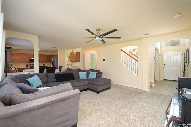 living area with stairway, light tile patterned floors, a ceiling fan, visible vents, and light colored carpet