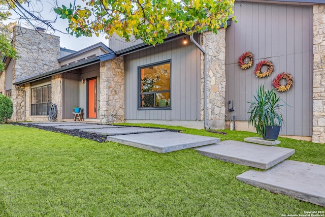 entrance to property featuring a yard, stone siding, and a chimney