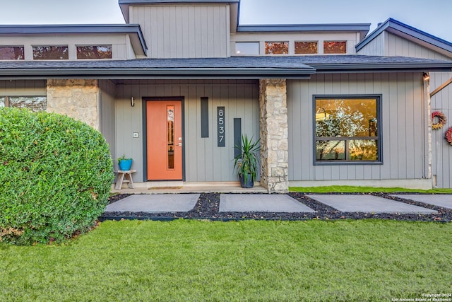 doorway to property featuring a yard and a shingled roof