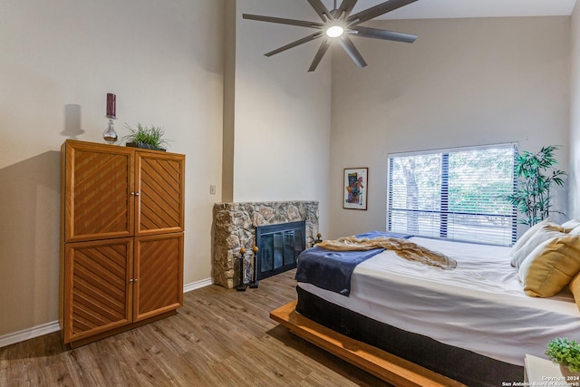 bedroom with baseboards, a stone fireplace, wood finished floors, and a towering ceiling