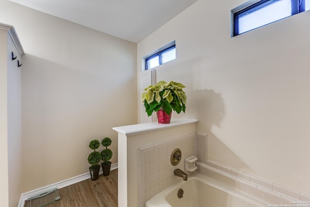 full bath with baseboards, wood finished floors, and a bath