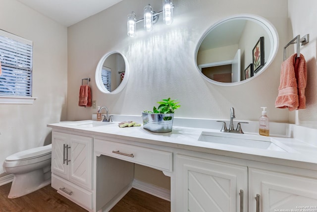 bathroom with double vanity, toilet, wood finished floors, and a sink