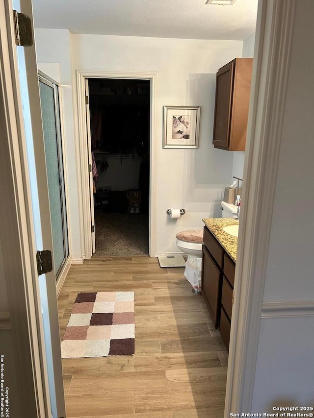 bathroom featuring a stall shower, a walk in closet, wood finished floors, and vanity