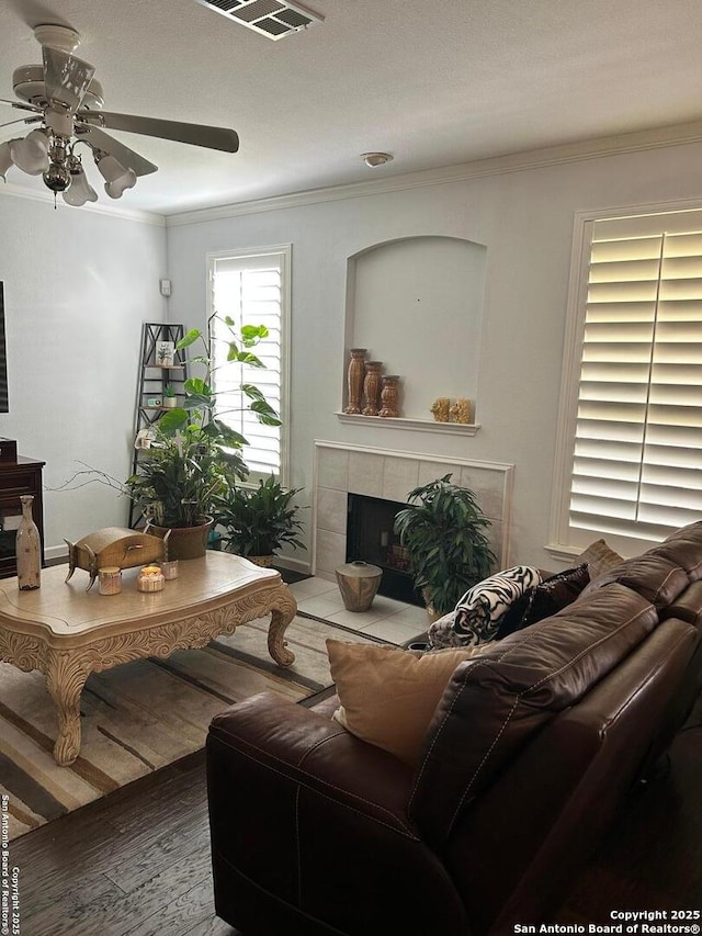 living room featuring wood finished floors, a fireplace, visible vents, and ornamental molding