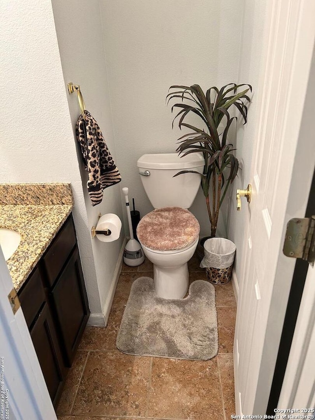 half bath featuring vanity, toilet, baseboards, and stone tile flooring