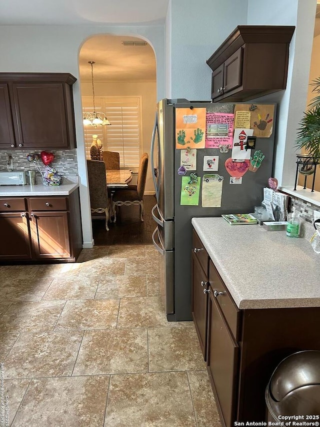 kitchen featuring freestanding refrigerator, dark brown cabinetry, stone finish floor, light countertops, and backsplash