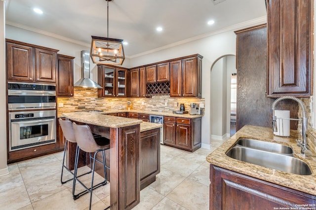 kitchen featuring wall chimney range hood, light stone countertops, double oven, arched walkways, and a sink