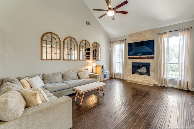 living room with visible vents, high vaulted ceiling, dark wood-type flooring, a tiled fireplace, and a ceiling fan