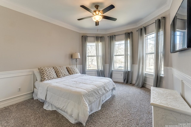 carpeted bedroom with wainscoting, crown molding, and a ceiling fan