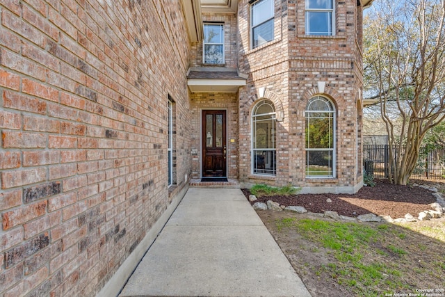 doorway to property featuring brick siding and fence