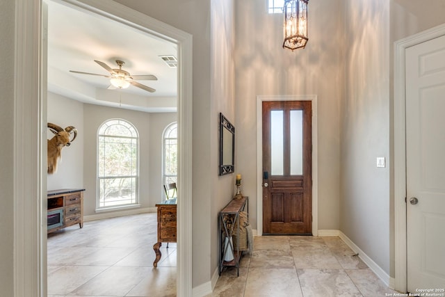 entrance foyer featuring baseboards, visible vents, a tray ceiling, light tile patterned flooring, and ceiling fan