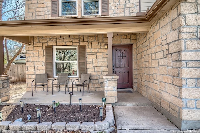 doorway to property with fence, covered porch, and stone siding