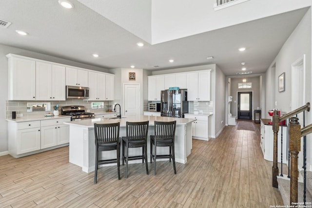 kitchen featuring a kitchen bar, light countertops, a kitchen island with sink, and appliances with stainless steel finishes