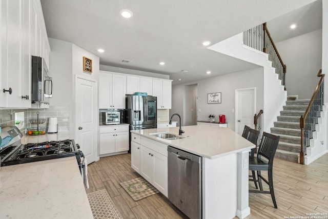 kitchen with tasteful backsplash, wood finish floors, appliances with stainless steel finishes, white cabinets, and a sink