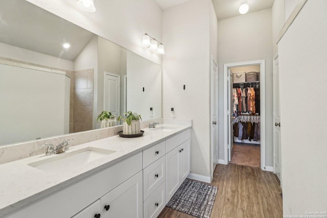 full bath featuring a sink, wood finished floors, double vanity, baseboards, and a spacious closet