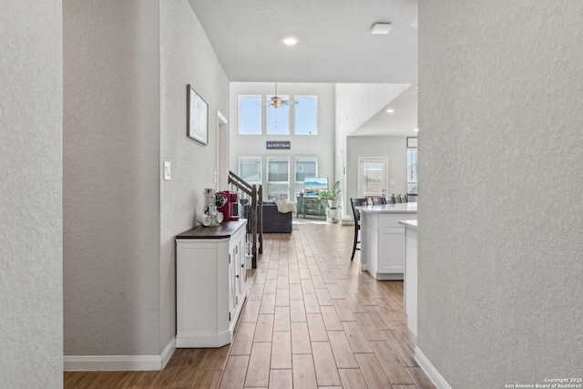 corridor with a textured wall, light wood-type flooring, baseboards, and stairway