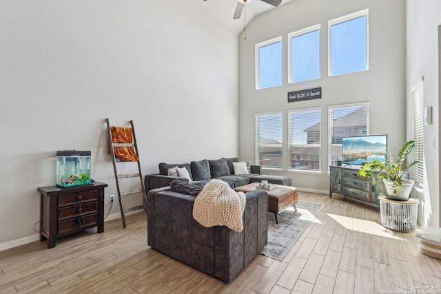 living area with light wood-style floors, baseboards, a towering ceiling, and ceiling fan