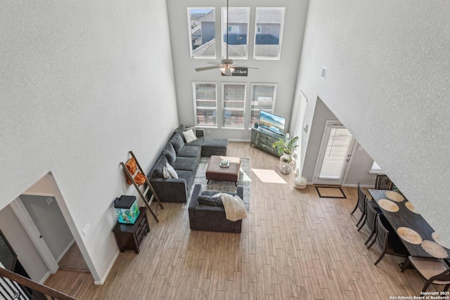 living room featuring ceiling fan, a high ceiling, baseboards, and wood finished floors