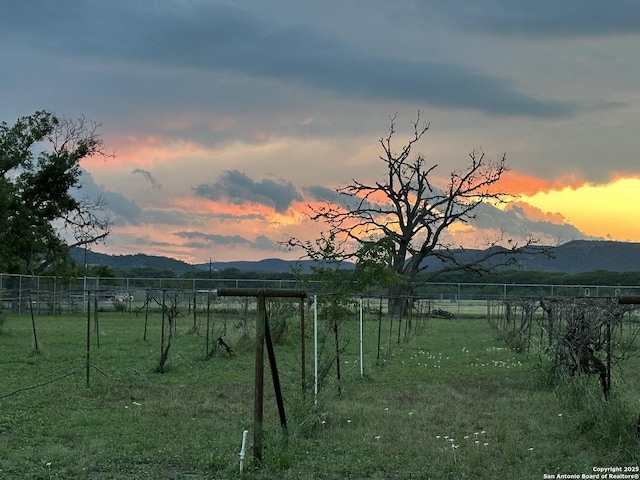 yard at dusk featuring a rural view, a mountain view, and fence