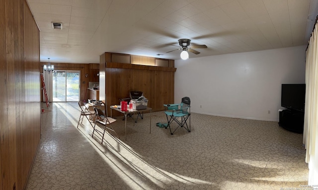 interior space featuring tile patterned floors, baseboards, wooden walls, and ceiling fan with notable chandelier