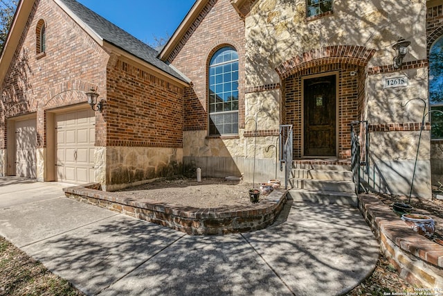 property entrance with stone siding, brick siding, an attached garage, and driveway