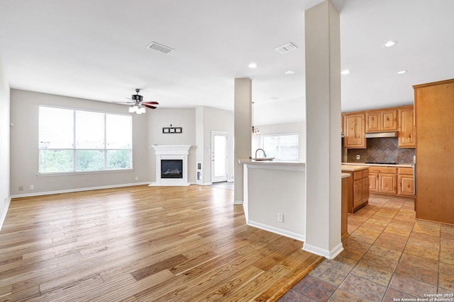 unfurnished living room featuring a glass covered fireplace, baseboards, visible vents, and a ceiling fan