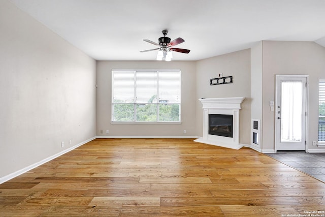 unfurnished living room with a glass covered fireplace, baseboards, light wood-style flooring, and a ceiling fan