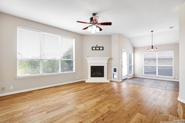 unfurnished living room with light wood-type flooring, visible vents, a glass covered fireplace, baseboards, and lofted ceiling