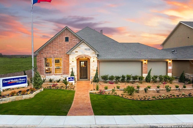 view of front of home with brick siding, a front yard, roof with shingles, a garage, and stone siding