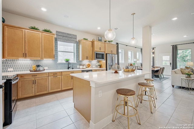 kitchen with a kitchen bar, a sink, tasteful backsplash, a center island, and appliances with stainless steel finishes