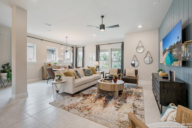 living area with light tile patterned floors, visible vents, ceiling fan with notable chandelier, and baseboards