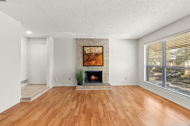 unfurnished living room featuring wood finished floors, baseboards, visible vents, a textured ceiling, and a brick fireplace