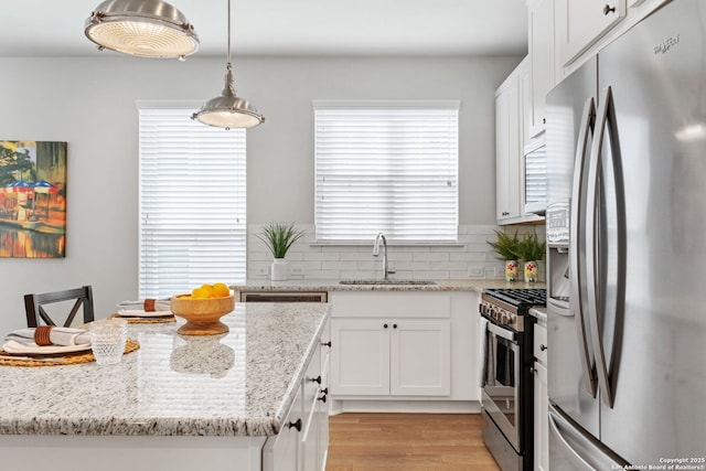 kitchen with light wood-style flooring, a sink, decorative backsplash, stainless steel appliances, and white cabinetry