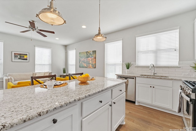 kitchen featuring decorative light fixtures, light wood-style floors, white cabinets, stainless steel appliances, and a sink