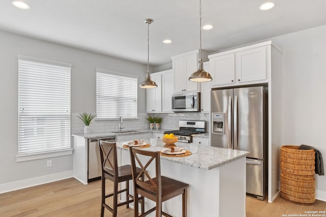 kitchen with tasteful backsplash, a kitchen island, hanging light fixtures, stainless steel appliances, and a sink