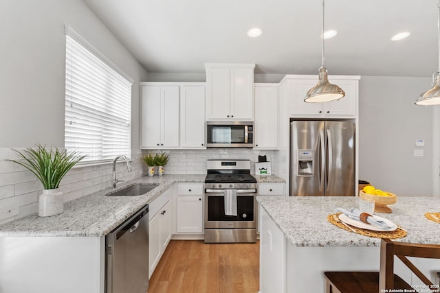 kitchen with light wood-type flooring, a sink, tasteful backsplash, stainless steel appliances, and white cabinets