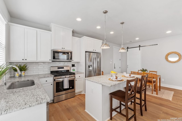 kitchen with a kitchen island, light wood-style flooring, a sink, stainless steel appliances, and a barn door