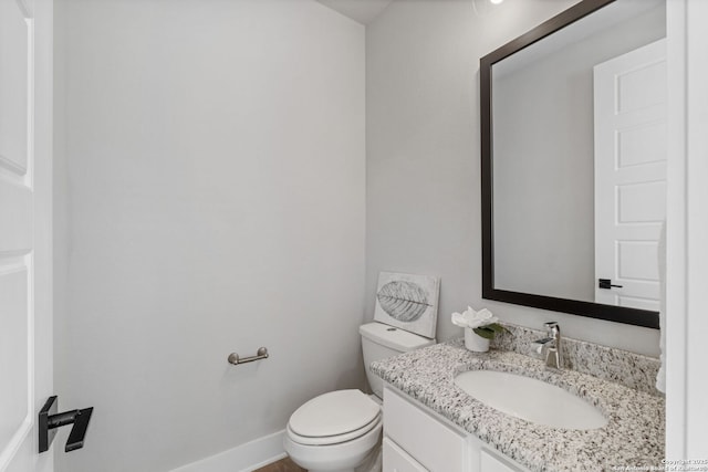 half bathroom featuring vanity, toilet, and baseboards