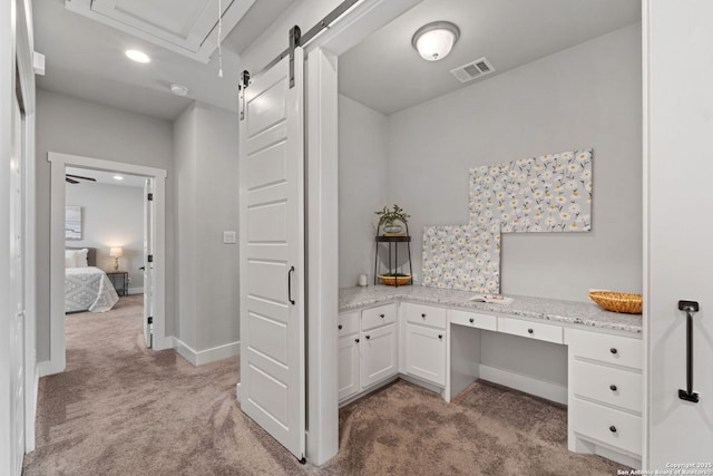 office area featuring visible vents, baseboards, a barn door, light carpet, and built in study area