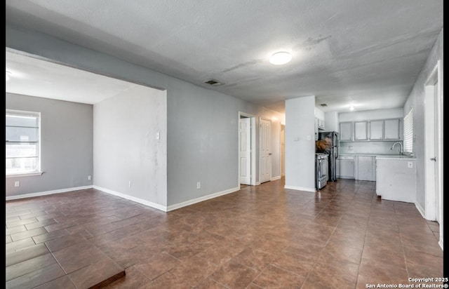 unfurnished living room with visible vents, baseboards, and a sink