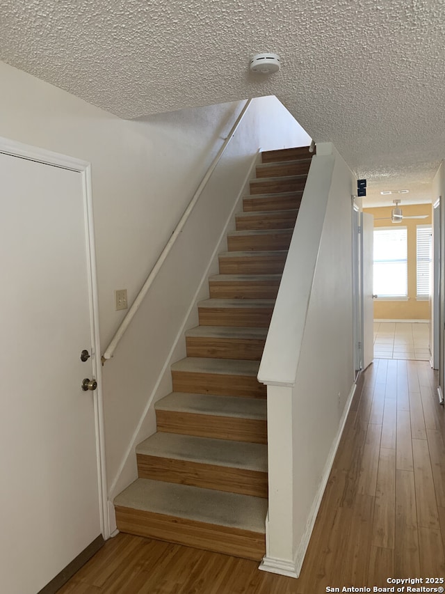 stairway with wood finished floors, baseboards, and a textured ceiling