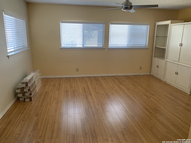 unfurnished bedroom with multiple windows, a textured ceiling, light wood-type flooring, and baseboards