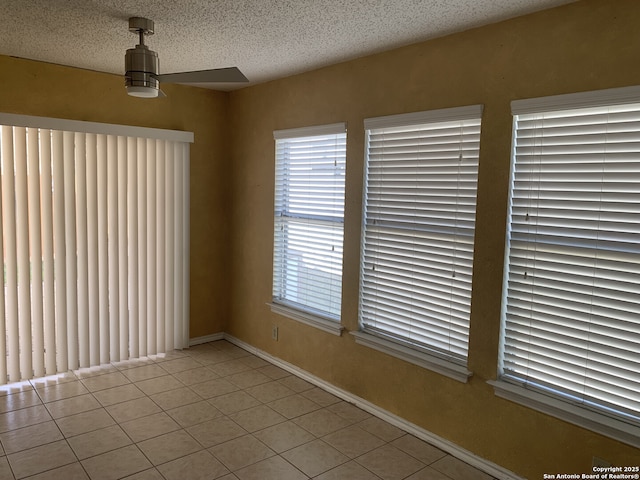 empty room featuring light tile patterned floors, a ceiling fan, baseboards, and a textured ceiling