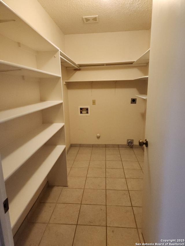 clothes washing area with washer hookup, a textured ceiling, light tile patterned floors, hookup for an electric dryer, and laundry area