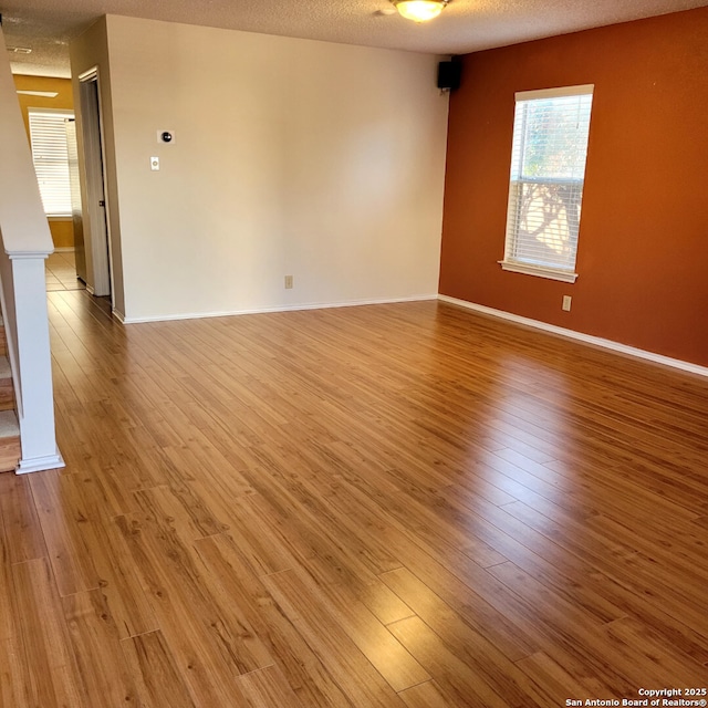 spare room with a textured ceiling, light wood-type flooring, and baseboards