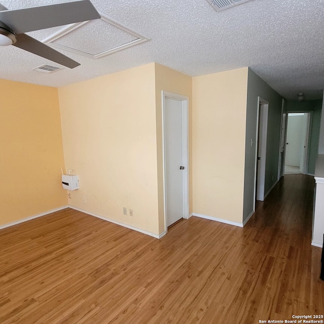 empty room featuring visible vents, baseboards, attic access, light wood-style floors, and a textured ceiling