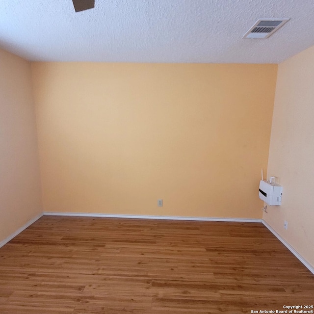 spare room featuring baseboards, wood finished floors, visible vents, and a textured ceiling