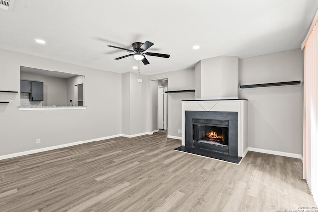 unfurnished living room with wood finished floors, baseboards, recessed lighting, a warm lit fireplace, and ceiling fan